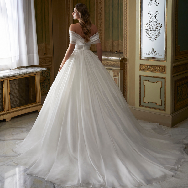 Back profile of model wearing Ronald Joyce style 69551, a beautiful ivory organdie ballgown wedding dress with ruched off the shoulder detail 